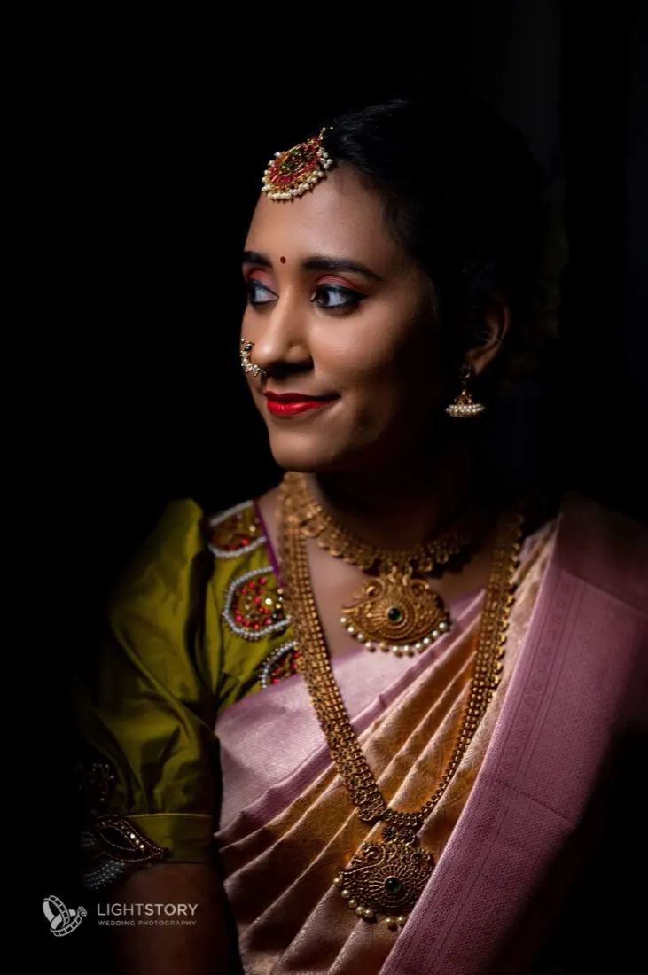 Bride in blush pattu and gold necklaces, turned to the light