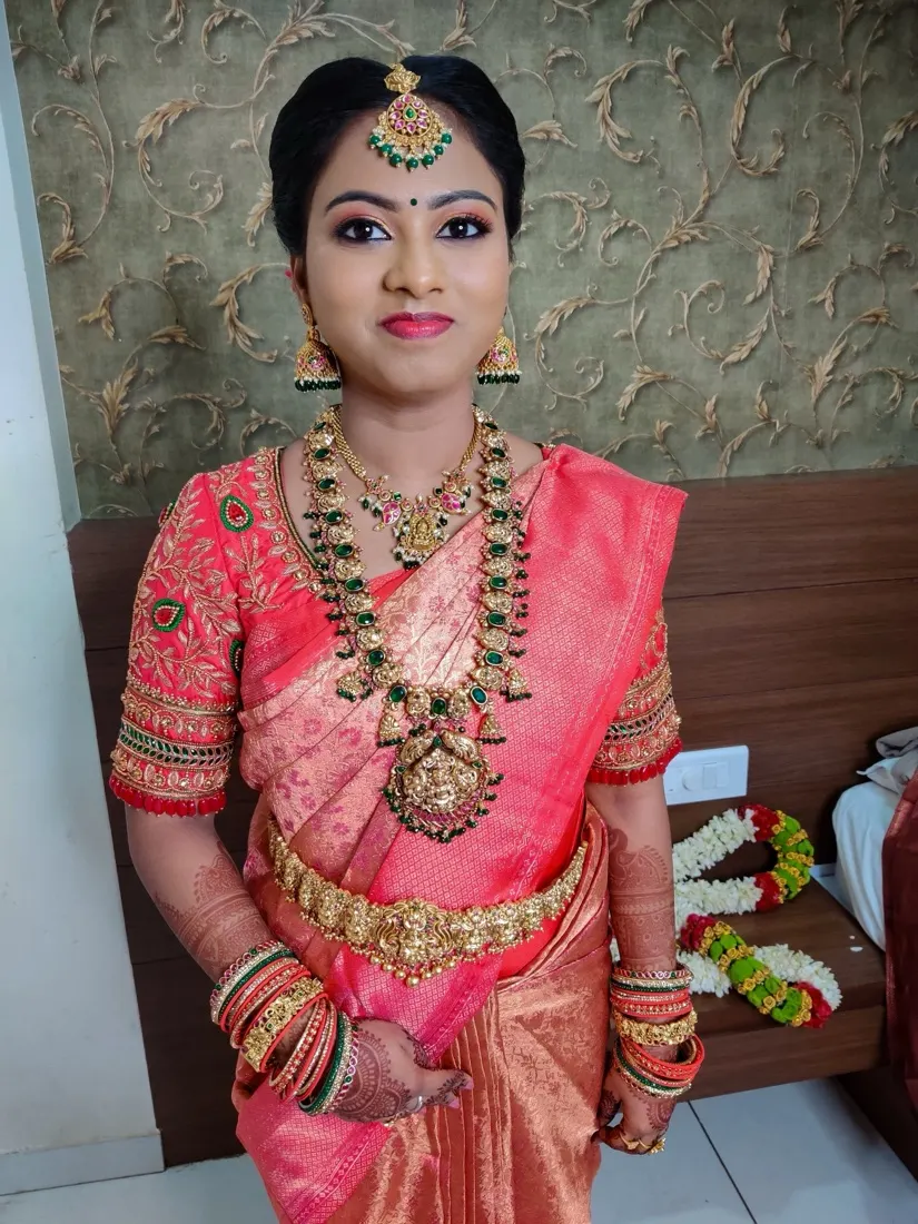 Bride in a coral silk saree with green-stone temple necklaces