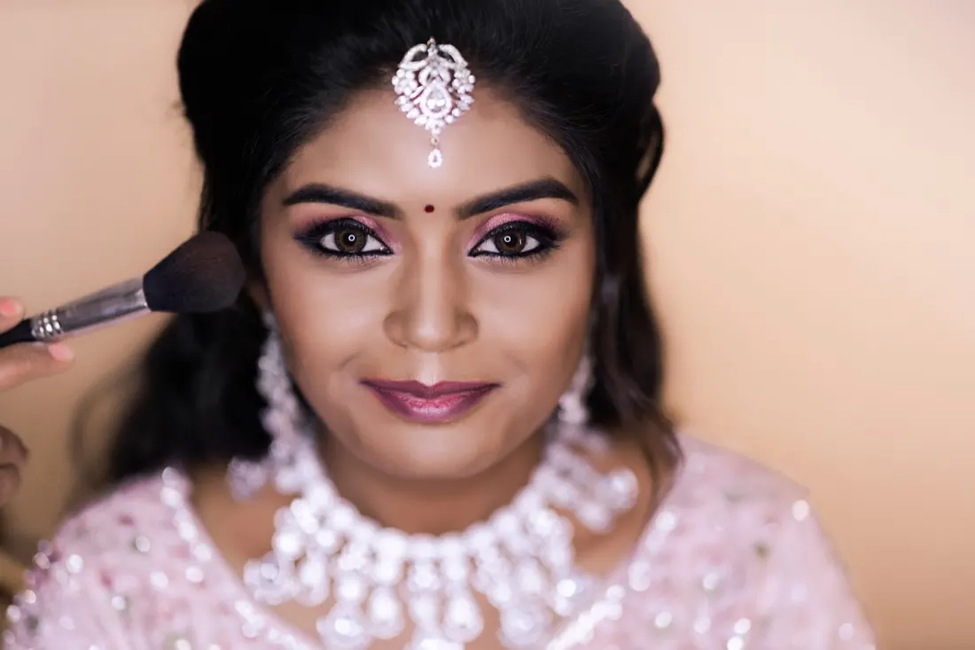 Keerthi blending blush on a bride wearing a crystal choker and maang tikka