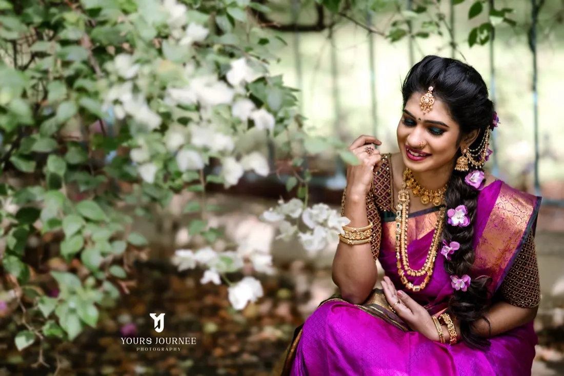 Bride in magenta silk seated among white flowers, smiling