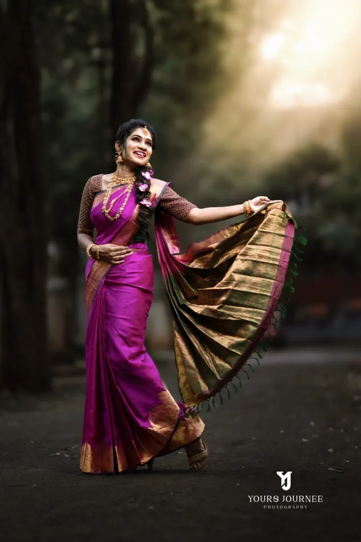 Bride swinging the pallu of a magenta silk saree on a forest path